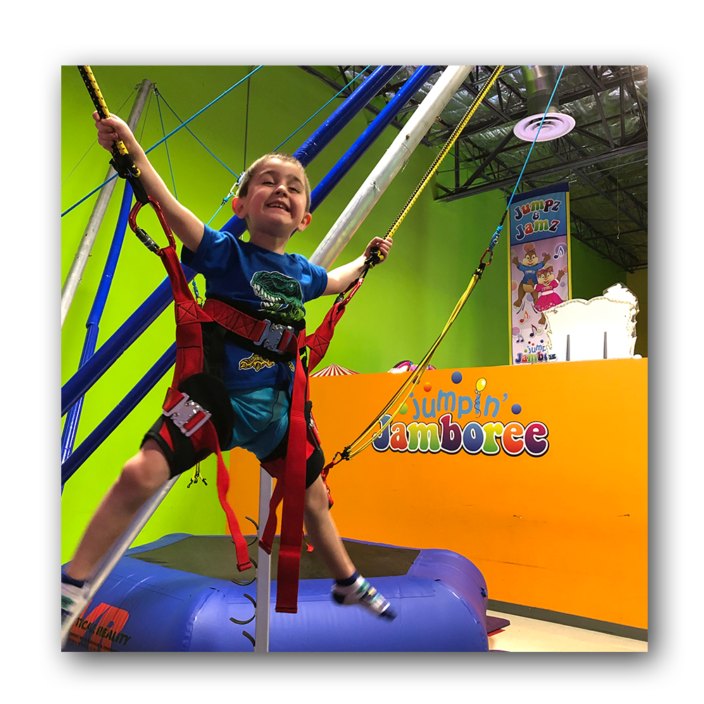 young boy in harness on jumping trampoline
